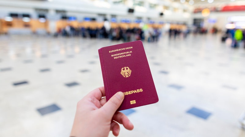 Hand hält deutschen Reisepass in Flughafenhalle