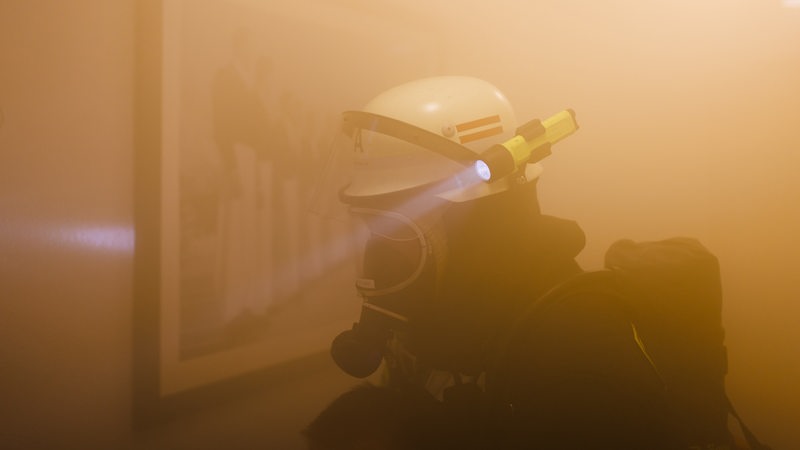 Ein Mitglied der Feuerwehr durchkämmt während einer Einsatzübung einer Freiwilligen Feuerwehr den künstlich vernebelten Innenraum eines Gebäudes.