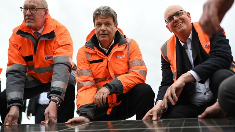 Der Vorstandschef der BLG,Wirtschaftsminister Habeck und Bürgermeister Bovenschulte knien hinter einer Solar-Anlage.