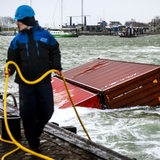 Ein Mann hält ein gelbes Seil, das an einem Container befestigt ist, der im Hafenbecken schwimmt