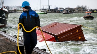 Ein Mann hält ein gelbes Seil, das an einem Container befestigt ist, der im Hafenbecken schwimmt