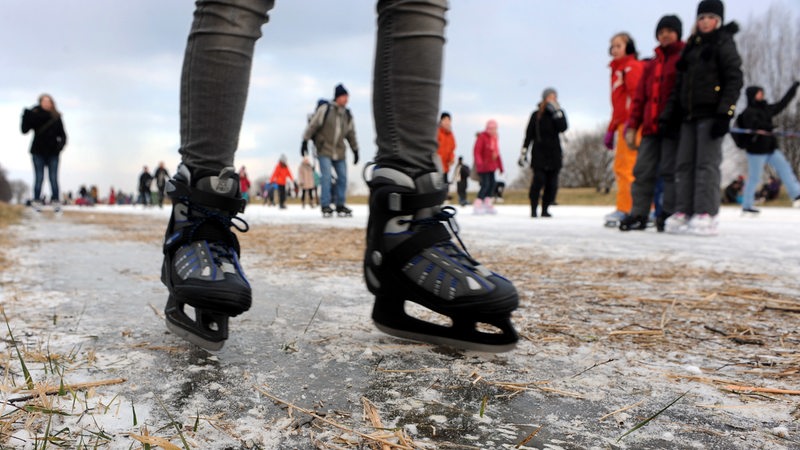 Eine Eisbahn in der Natur, Menschen fahren darauf mit Schlittschuhen