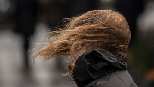 Starker Wind lässt die Haare einer Frau wehen, sodass ihr Gesicht von Haaren bedeckt ist