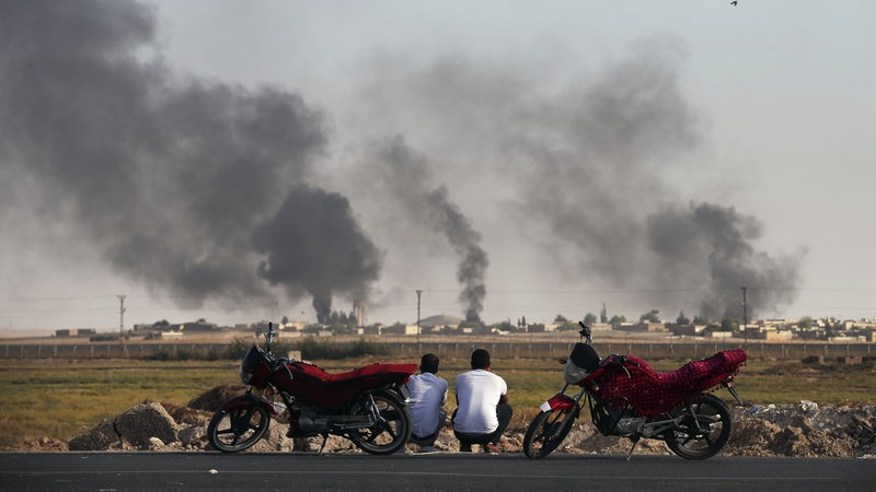 Zwei Männer blicken auf aufsteigenden Rauch über der nordsyrischen Provinz Sanliurfa