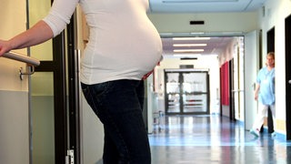 Eine schwangere Frau steht auf dem Flur einer Geburtsstation in einem Krankenhaus.