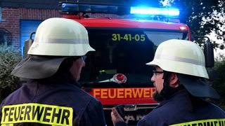 Zwei Feuerwehrleute stehen vor einem Feuerwehrauto.