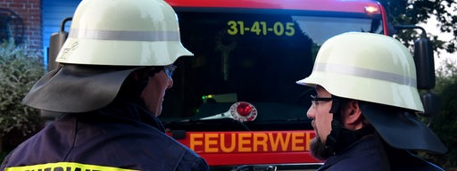 Zwei Feuerwehrleute stehen vor einem Feuerwehrauto.