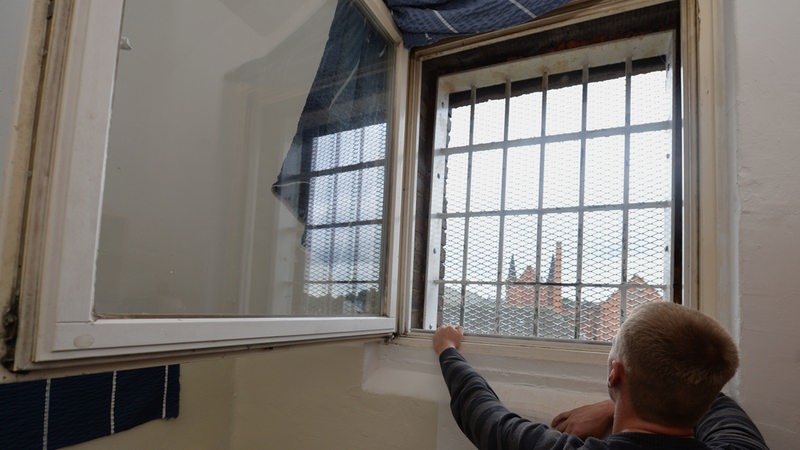 Häftling schaut aus durch die Gitter seines Fensters