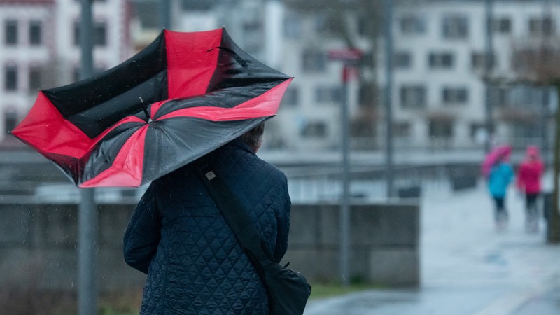 Frau läuft mit einem Regenschirm durch den Regen und Wind