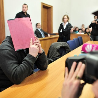 Der ehemalige Krankenpfleger Niels Högel versteckt sein Gesicht hinter einem Aktendeckel, während er auf der Anklagebank des Landgerichts in Oldenburg sitzt