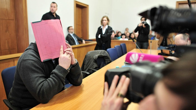 Der ehemalige Krankenpfleger Niels Högel versteckt sein Gesicht hinter einem Aktendeckel, während er auf der Anklagebank des Landgerichts in Oldenburg sitzt