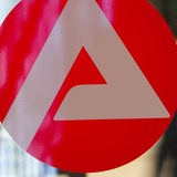 Eine Frau geht in der Bundesagentur für Arbeit in Frankfurt am Main an einem Logo der Arbeitsagentur vorbei.