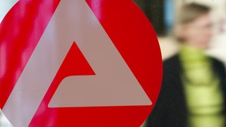 Eine Frau geht in der Bundesagentur für Arbeit in Frankfurt am Main an einem Logo der Arbeitsagentur vorbei.