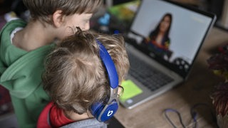 Kinder sitzen vor einem Computer und sprechen mit einer Frau (Symbolbild)