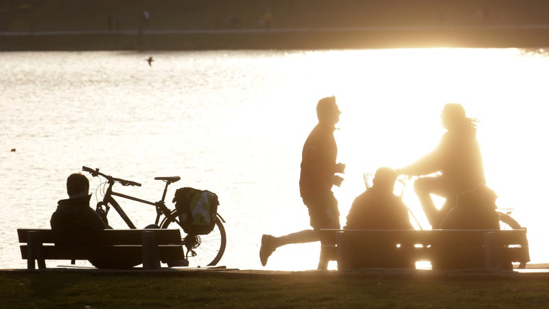 Menschen auf Fahrrädern und Parkbänken im Gegenlicht.