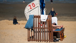 Aus einem Strandkorb gucken mehrere Beine, im Hintergrund spielen Kinder.