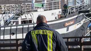 Ein Feuerwehrmann steht vor dem am Alten Hafen liegenden Traditionssegler "Seute Deern", auf dem in der Nacht zuvor ein Großbrand ausgebrochen ist.