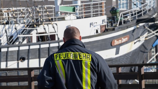Ein Feuerwehrmann steht vor dem am Alten Hafen liegenden Traditionssegler "Seute Deern", auf dem in der Nacht zuvor ein Großbrand ausgebrochen ist.