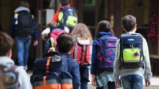  Schülerinnen und Schüler gehen vom Schulhof hintereinander ins Schulgebäude.