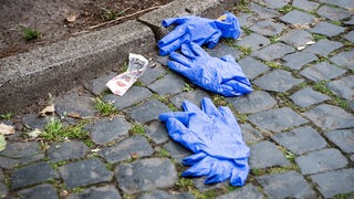 Einweghandschuhe liegen neben einer Plastikverpackung auf Kopfsteinpflaster.