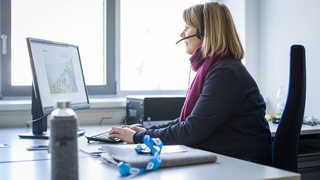 Eine Frau sitzt vor einem Computer und hat ein Headset auf dem Kopf.