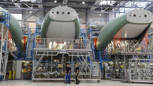 Mitarbeiter von Airbus gehen in einer Fertigungshalle am Rumpf des A400M entlang.