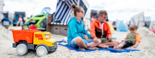 Ein Spielzeug-LKW steht im Sand vor dem Strandkorb einer Familie am Nordstrand Norderney.