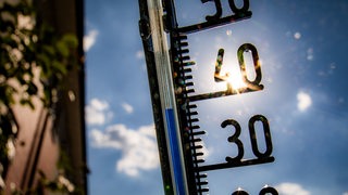 Ein analoges Thermometer, das über 30 Grad zeigt, wird gegen die Sonne gehalten.