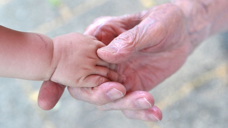 Die Hand eines alten Menschen hält die Hand eines Babys.