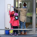 Eine Mutter mit zwei Kindern klingelt an einer Tür zu einer Kita.