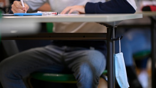 Ein Schüler sitzt am Platz, am Tisch hängt seine Schutzmaske. (Symbolbild)