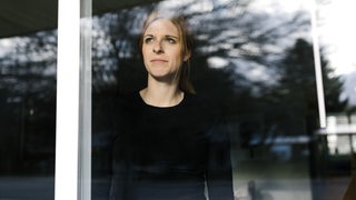 Eine Frau steht hinter einem Fenster und schaut hinaus (Symbolbild)