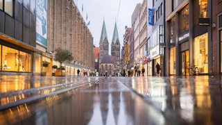 Der Bremer St. Petri Dom spiegelt sich auf dem nassen Pflaster der Bremer Fußgängerzone.