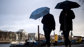 Zwei Menschen laufen mit Regenschirmen in der Hand am Weserufer in Bremen entlang.