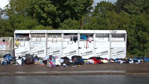 Vollgestopfte Altkleidercontainer stehen am Straßenrand.