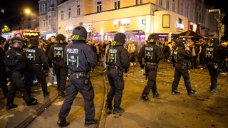 Polizisten in Schutzanzügen laufen über den Sielwall, während Fans von Werder Bremen nach dem Spiel am 06.07.2020 auf der Straße jubeln. 
