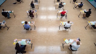 Schülerinnen und Schüler sitzen während einer Abiturprüfung mit dem vorgeschriebenen Abstand zueinander in der Aula eines Gymnasiums. 