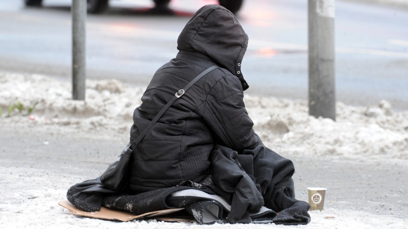 Ein Obdachloser sitzt auf der Straße.