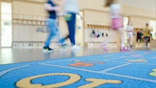 Hinter einem Teppich mit bunten Zahlen laufen Kinder auf dem Flur eines städtischen Kindergartens. 