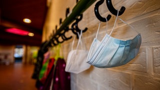 Masken und Jacken hängen im Flur einer Schule an Kleiderhaken
