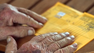 Die faltigen Hände eines alten Mannes liegen auf seinem Impfausweis, in dem die Impfung gegen Sars-CoV-2 eingetragen ist.