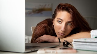 Eine Studentin im Home-Office schaut verzweifelt und erschöpft auf ihren Laptop