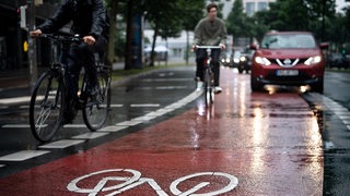 Auf einer regennassen Straße fährt ein Radfahrer auf einem roten Radweg neben einem Auto.