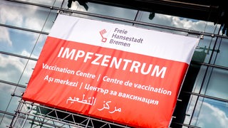 Ein Schild mit der Aufschrift „Impfzentrum“ in mehreren Sprachen hängt über dem Eingang des Impfzentrums in der Messehalle an der Bürgerweide.