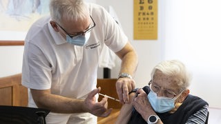 Ein Hausarzt impft eine ältere Frau gegen das Coronavirus.