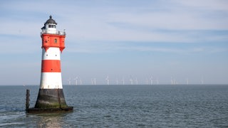 Ein rot-weiß-gestreifter Leuchtturm steht im Meer.