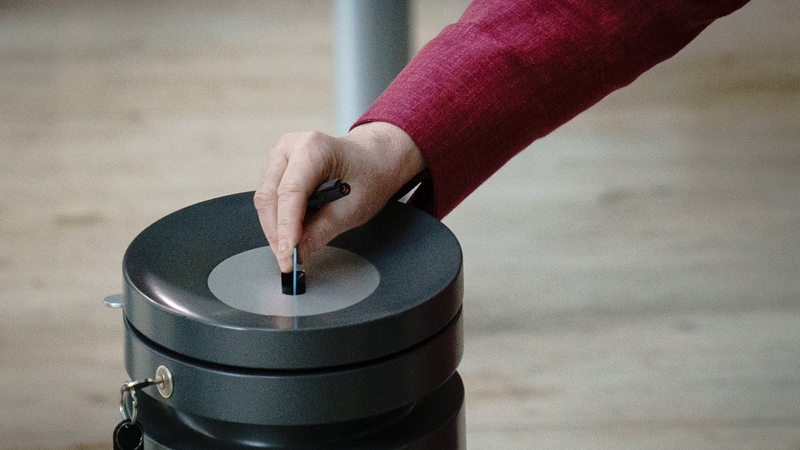 Eine Hand steckt eine Stimmkarte im Bundestag in die Wahlurne