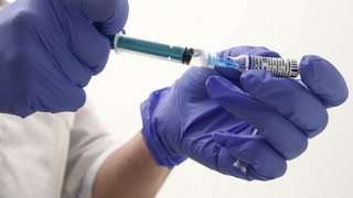 Zwei Hände in blauen Handschuhen halten eine Spritze und ein Fläschen mit einer Impfdose.