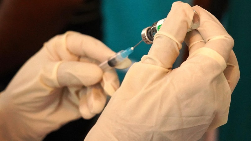Zwei Hände in weißen Handschuhen halten eine Impfampulle und eine Spritze in den Händen.