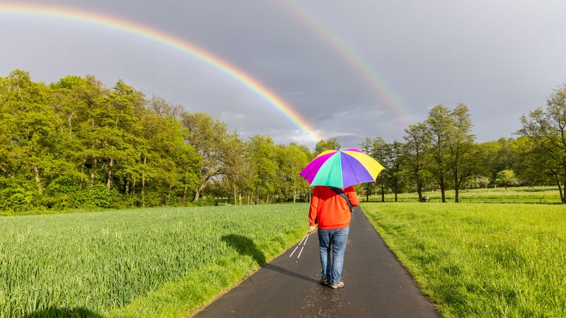 Ein Regenbogen ist am späten Nachmittag hinter einem Regenschauer über den Wiesen am Stadtrand zu sehen.